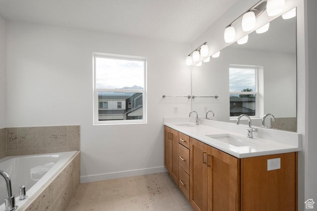 bathroom with double vanity, plenty of natural light, tiled tub, and baseboards