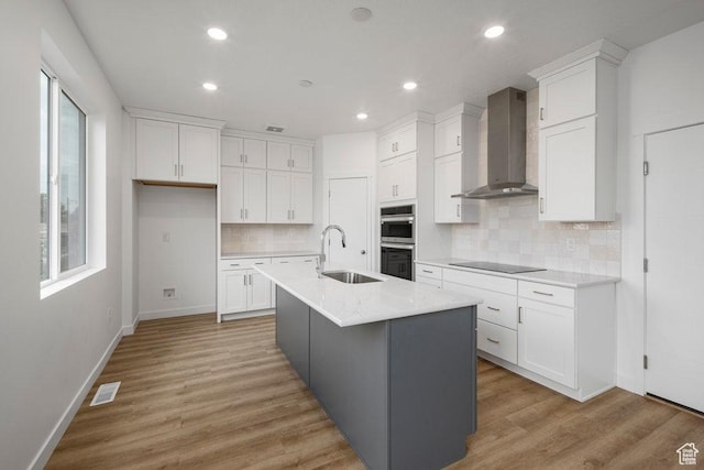 kitchen featuring wall chimney range hood, a sink, double oven, black electric cooktop, and white cabinets