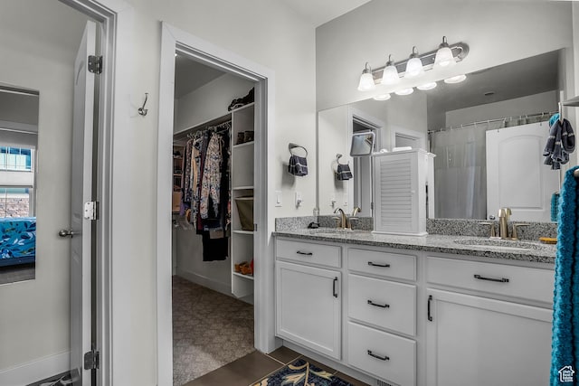 bathroom with double vanity, a spacious closet, a sink, and tile patterned floors