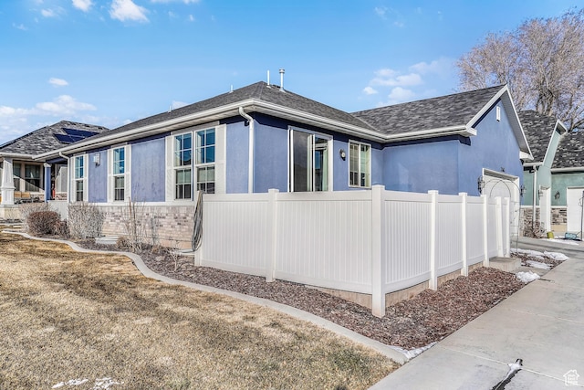 view of side of home with a shingled roof, fence, and stucco siding