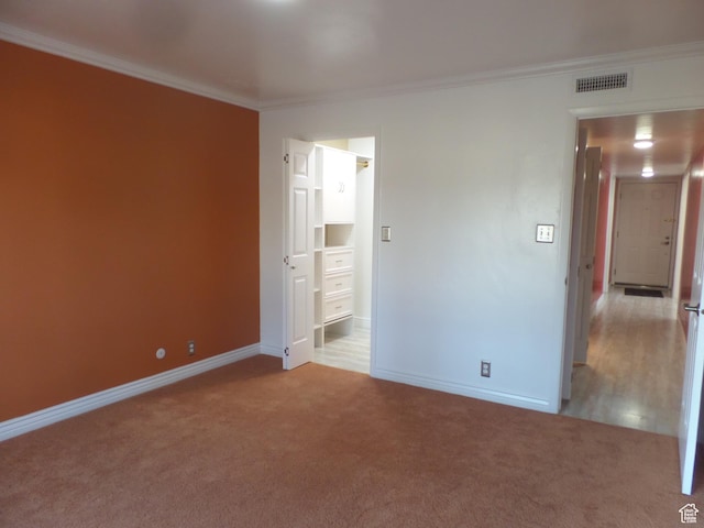 unfurnished bedroom featuring crown molding, ensuite bath, and light carpet