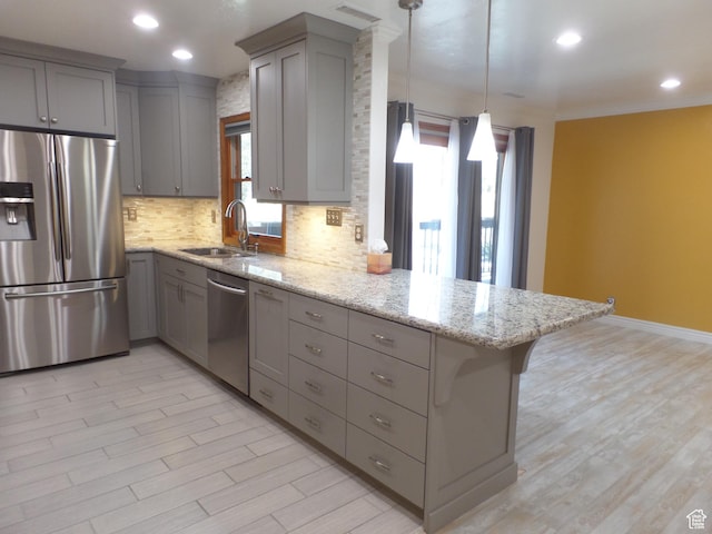 kitchen with pendant lighting, sink, appliances with stainless steel finishes, light stone counters, and kitchen peninsula