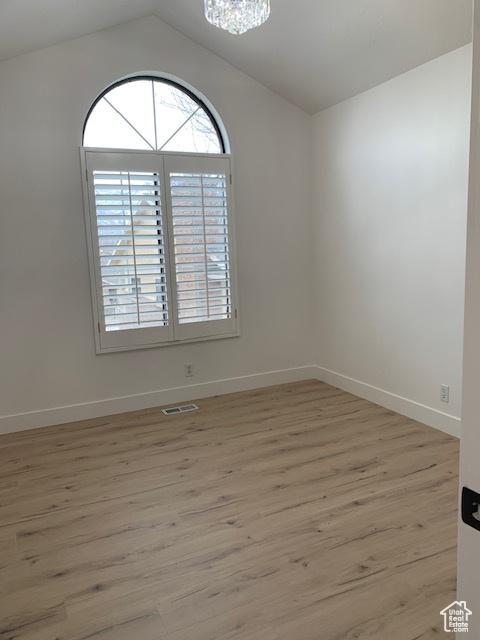 unfurnished room with lofted ceiling, a chandelier, and light hardwood / wood-style flooring