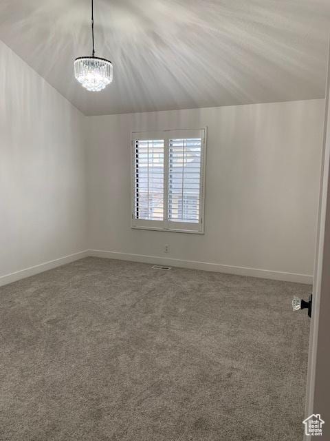 empty room with carpet flooring, a chandelier, and vaulted ceiling
