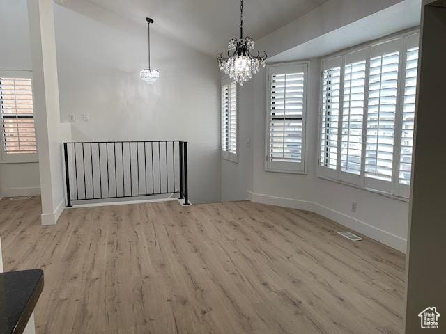 unfurnished dining area featuring plenty of natural light, lofted ceiling, an inviting chandelier, and light hardwood / wood-style flooring