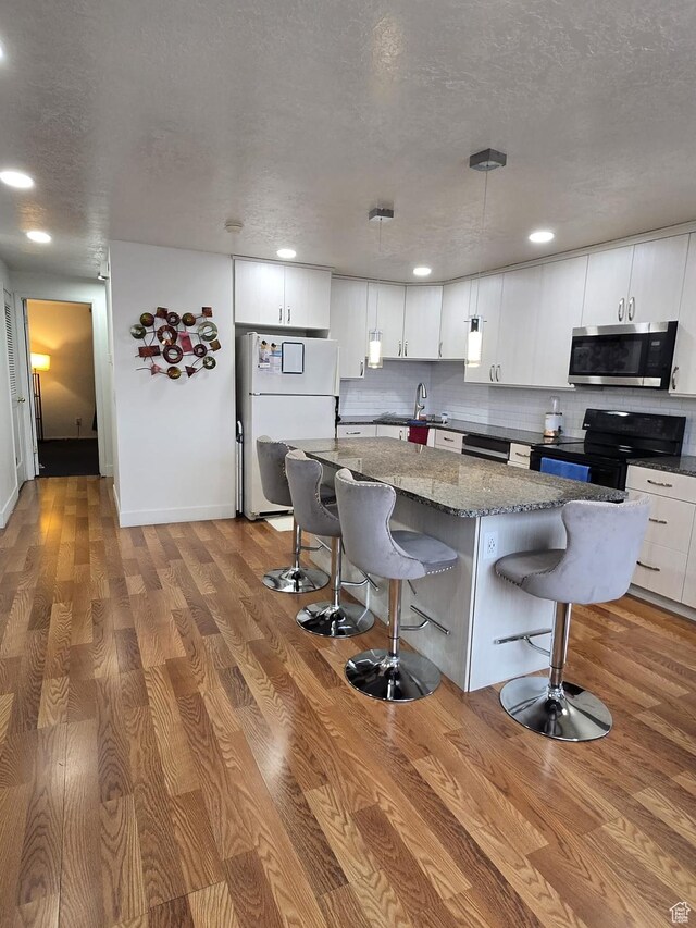 3673 S 2200th St W Unit 13, West Valley City, UT 84119 - kitchen with a breakfast bar, white cabinetry, a kitchen island, light hardwood / wood-style floors, and black appliances