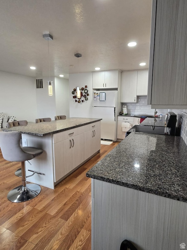 3673 S 2200th St W Unit 13, West Valley City, UT 84119 - kitchen featuring light hardwood / wood-style flooring, white cabinetry, a kitchen breakfast bar, white refrigerator, and decorative light fixtures