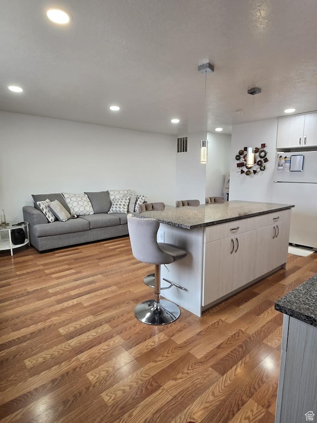 3673 S 2200th St W Unit 13, West Valley City, UT 84119 - kitchen with white cabinetry, wood-type flooring, hanging light fixtures, a kitchen breakfast bar, and a kitchen island
