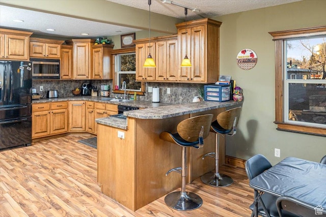 kitchen with black fridge, hanging light fixtures, a textured ceiling, stainless steel microwave, and kitchen peninsula
