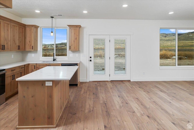kitchen with decorative light fixtures, dishwasher, a center island, light stone counters, and light wood-type flooring