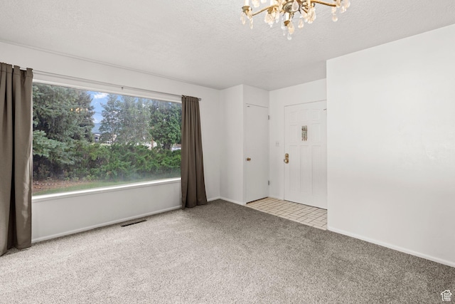 carpeted spare room with a chandelier and a textured ceiling