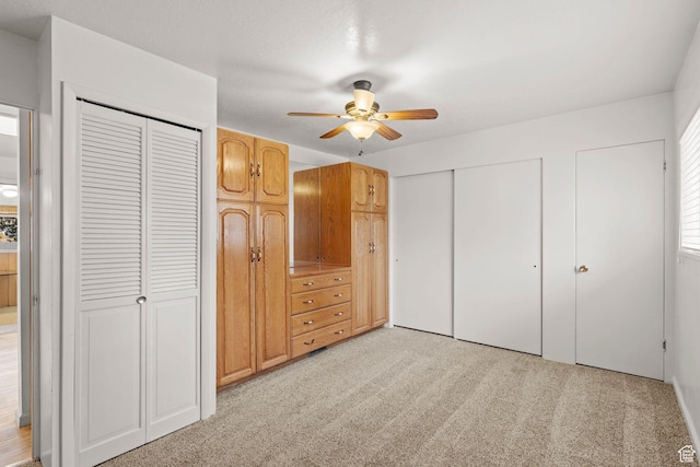 unfurnished bedroom featuring two closets, light colored carpet, and ceiling fan