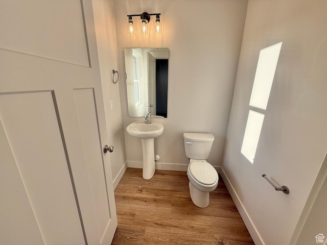 half bath featuring a sink, toilet, baseboards, and wood finished floors