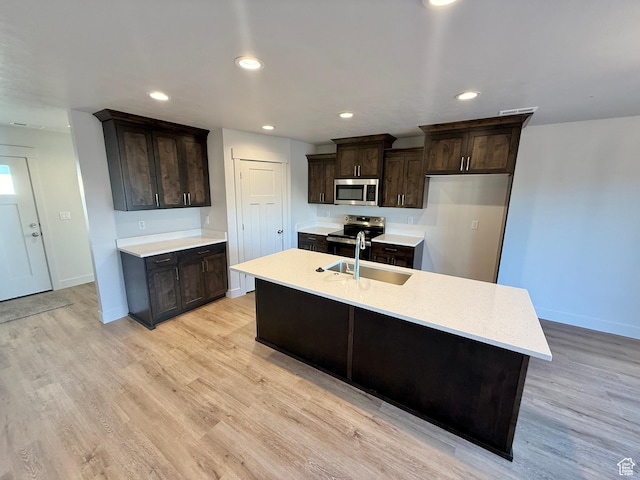 kitchen with a sink, stainless steel appliances, light countertops, dark brown cabinets, and light wood-style floors