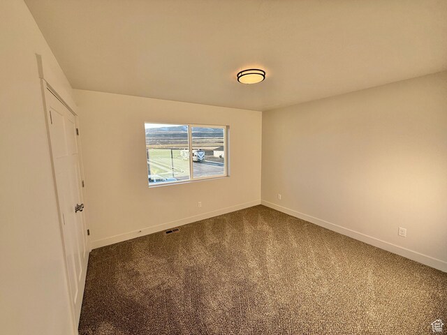 unfurnished room featuring dark colored carpet, visible vents, and baseboards