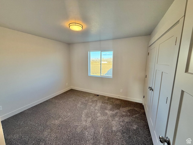 unfurnished bedroom featuring baseboards and dark carpet