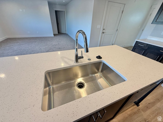 kitchen featuring carpet flooring, light stone countertops, baseboards, and a sink