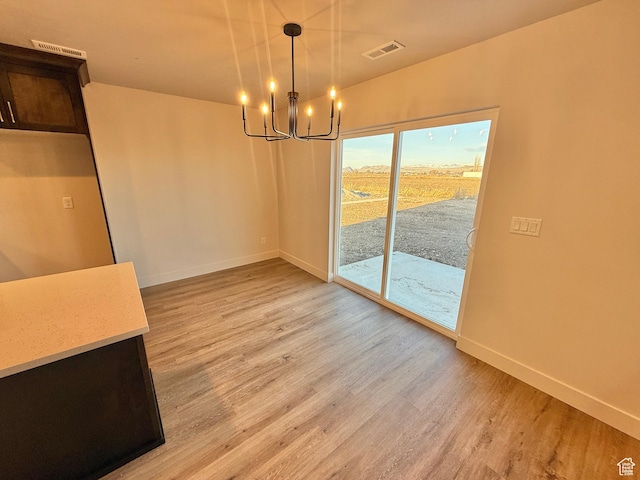 unfurnished dining area featuring a notable chandelier, baseboards, visible vents, and light wood finished floors