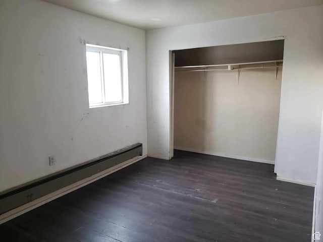 unfurnished bedroom with baseboard heating, dark hardwood / wood-style flooring, and a closet