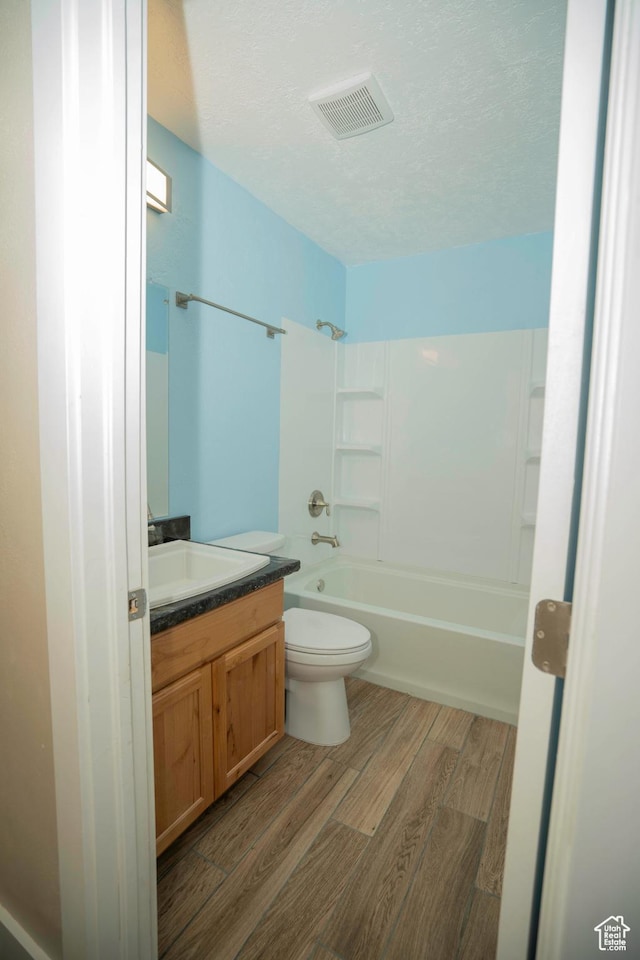full bathroom featuring wood-type flooring, washtub / shower combination, vanity, toilet, and a textured ceiling