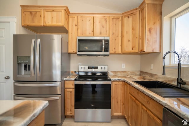 kitchen featuring sink, appliances with stainless steel finishes, light stone countertops, light brown cabinetry, and vaulted ceiling
