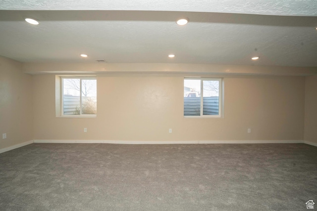 spare room featuring a textured ceiling and dark colored carpet