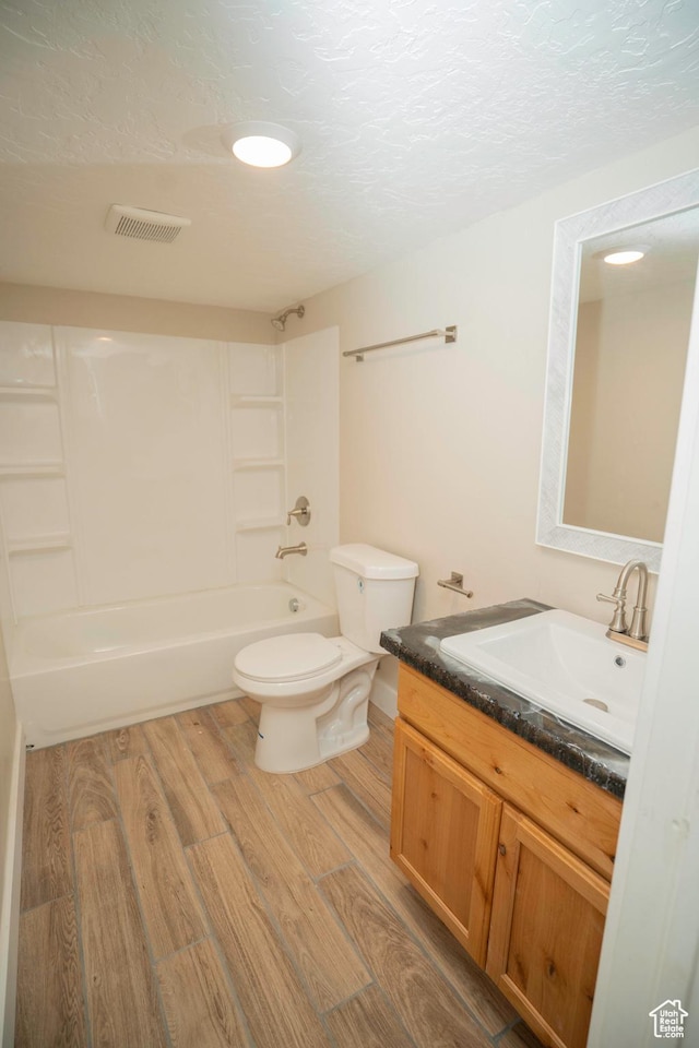 full bathroom with hardwood / wood-style floors, vanity, a textured ceiling, shower / washtub combination, and toilet