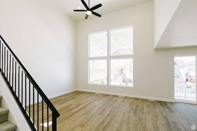 unfurnished living room with baseboards, a ceiling fan, stairs, and wood finished floors