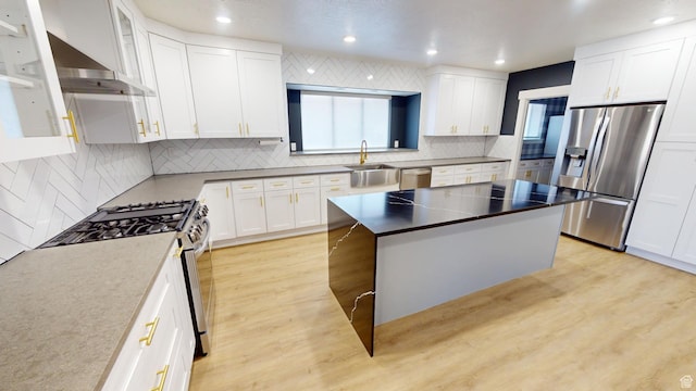 kitchen with appliances with stainless steel finishes, white cabinetry, sink, a center island, and light hardwood / wood-style floors