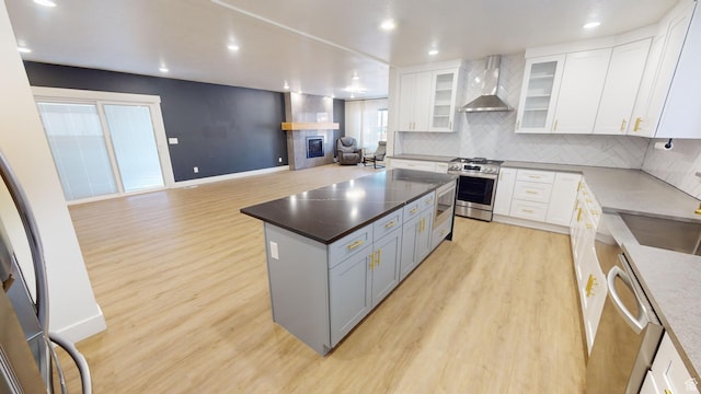 kitchen with stainless steel appliances, a kitchen island, white cabinets, and wall chimney exhaust hood