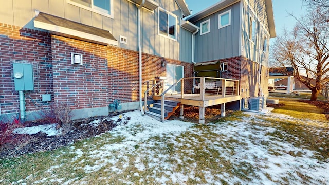 snow covered property with central AC unit and a deck
