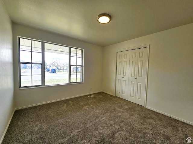 unfurnished bedroom with baseboards, a closet, and dark colored carpet