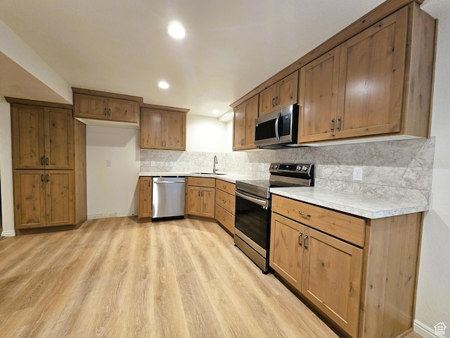 kitchen with light countertops, stainless steel appliances, backsplash, a sink, and light wood-style floors