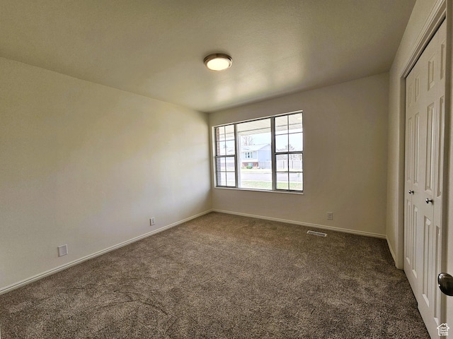 unfurnished bedroom with a closet, baseboards, visible vents, and dark carpet