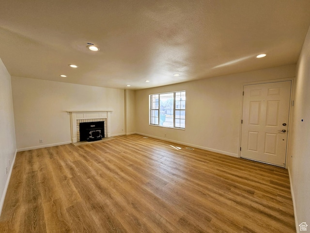 unfurnished living room with baseboards, a fireplace, recessed lighting, and light wood finished floors