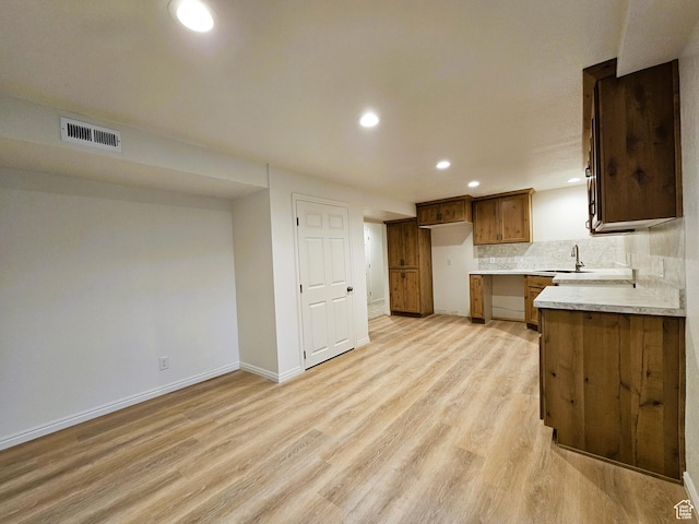 kitchen with light countertops, a sink, tasteful backsplash, light wood-style flooring, and visible vents