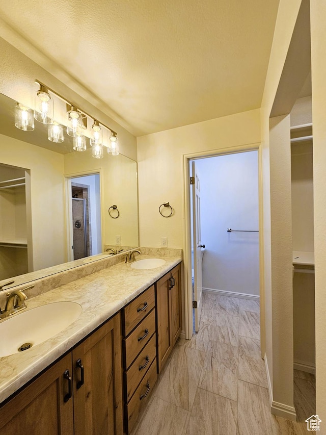 full bath with marble finish floor, double vanity, a walk in closet, and a sink