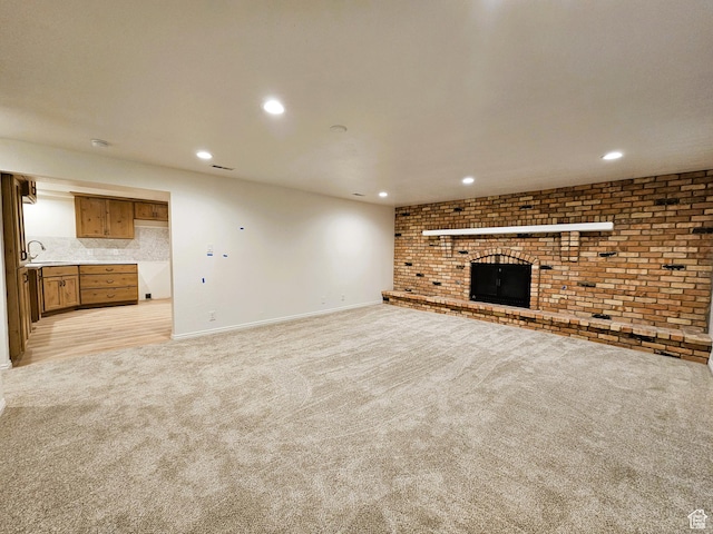 unfurnished living room featuring a sink, light carpet, a fireplace, baseboards, and recessed lighting