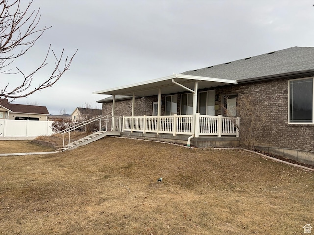 exterior space with covered porch, brick siding, a shingled roof, fence, and a yard