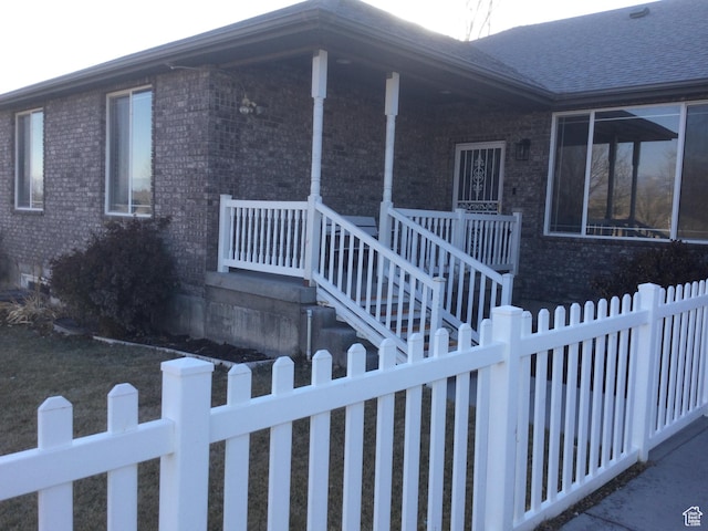 view of front facade featuring a porch, brick siding, and a fenced front yard