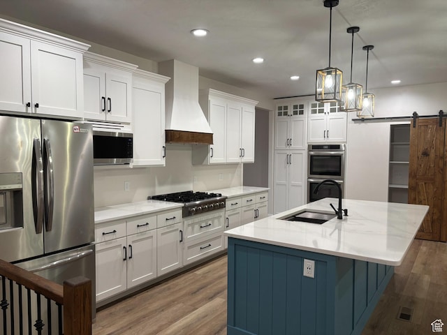 kitchen with a barn door, premium range hood, a sink, white cabinetry, and appliances with stainless steel finishes