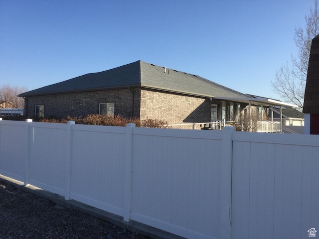 view of home's exterior with brick siding, a shingled roof, and fence
