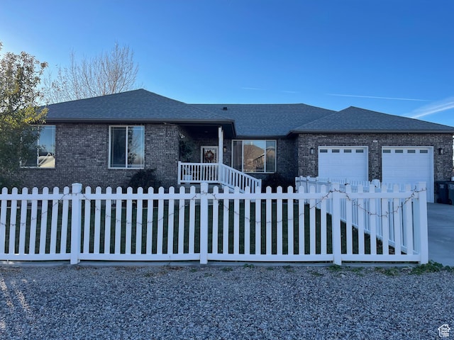 ranch-style home featuring a fenced front yard, brick siding, roof with shingles, an attached garage, and driveway