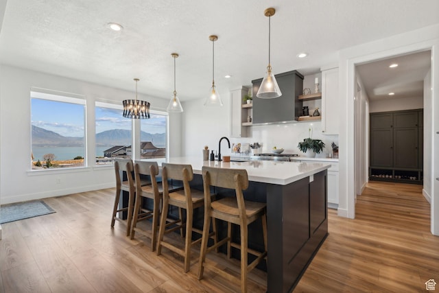 kitchen with decorative light fixtures, an island with sink, light hardwood / wood-style flooring, and white cabinets