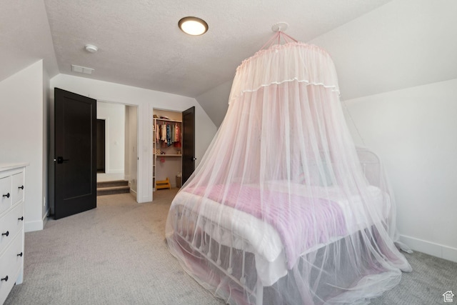 carpeted bedroom with a walk in closet, vaulted ceiling, and a textured ceiling