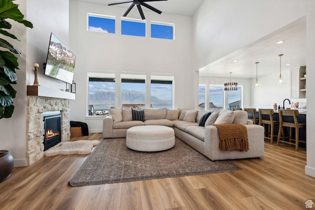living room featuring a stone fireplace, sink, hardwood / wood-style flooring, a towering ceiling, and ceiling fan with notable chandelier