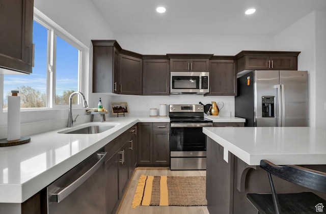 kitchen with sink, a breakfast bar, appliances with stainless steel finishes, dark brown cabinetry, and light hardwood / wood-style floors