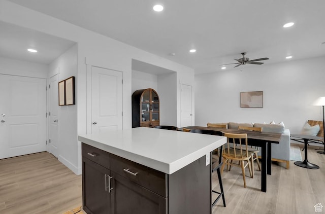 kitchen featuring ceiling fan, dark brown cabinets, a kitchen breakfast bar, light hardwood / wood-style floors, and a kitchen island