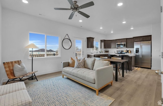 living room featuring ceiling fan, sink, and light wood-type flooring