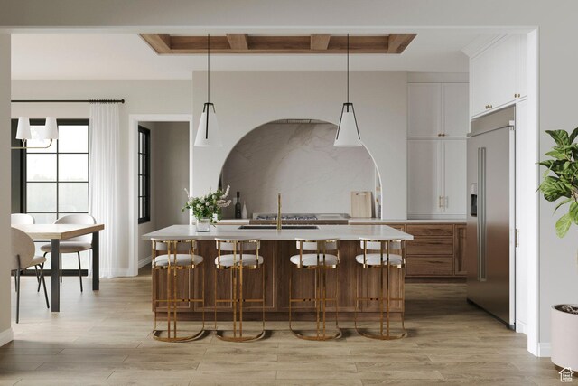kitchen featuring light wood finished floors, a sink, light countertops, built in fridge, and a kitchen breakfast bar